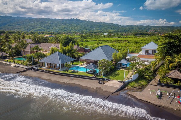 A coastal property with a swimming pool, beachfront, and lush greenery.