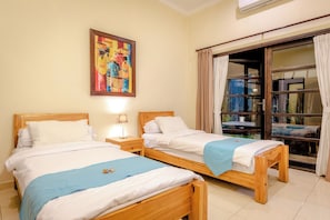 A room with two wooden beds, a nightstand with a lamp, a painting on the wall, and a sliding glass door leading to an outdoor area. - Beachfront pool villa: Free welcome dinner! With own boat! (Dencarik)