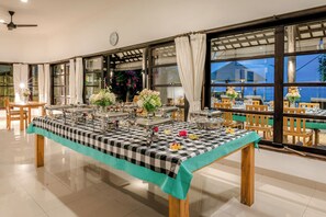 A dining area with a checkered tablecloth, multiple tables, and chairs, with large windows and curtains. - Luxury 6BR Beachfront Villa with Private Pool! (Dencarik)