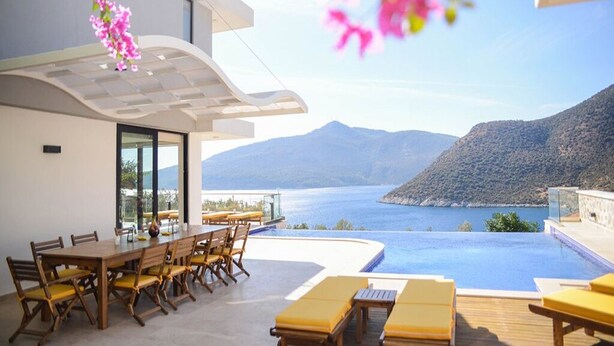 A modern outdoor dining area with a pool overlooking a scenic mountain and sea view.