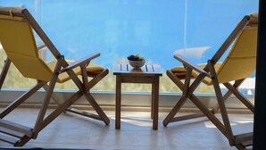 Two yellow lounge chairs facing a table with a bowl of fruit, set on a balcony with a view of the sea.