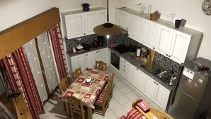 Una cocina compacta con armarios blancos, una mesa de comedor con mantel rojo y blanco estampado, y un refrigerador.