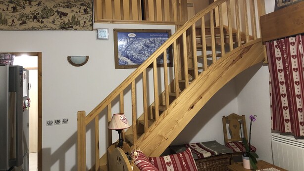 Una escalera de madera en una habitación con un cuadro enmarcado de una montaña nevada, una lámpara y una pequeña mesa con una planta.