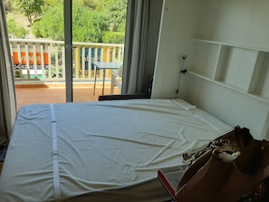 A room with a bed, a small table, and a view of a balcony with a railing and greenery. - Comfortable, serene studio in residence, swimming pool, tennis court, private parking, terrace. (Sausset-les-Pins)