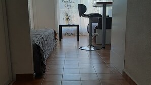 A small, compact room with a bed, a desk, and a chair. There is a window with a view of trees and a building outside.