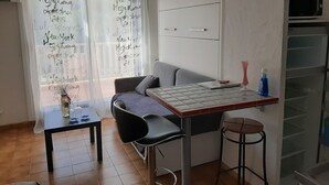 A compact living space with a kitchenette, a sofa, a small dining table, and a bar stool.