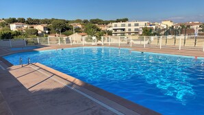 A swimming pool with a tiled deck, metal handrails, and a white fence.