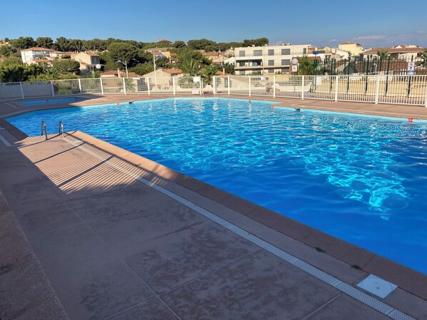 Una piscina con solárium empavedado, barandillas metálicas y una valla blanca.