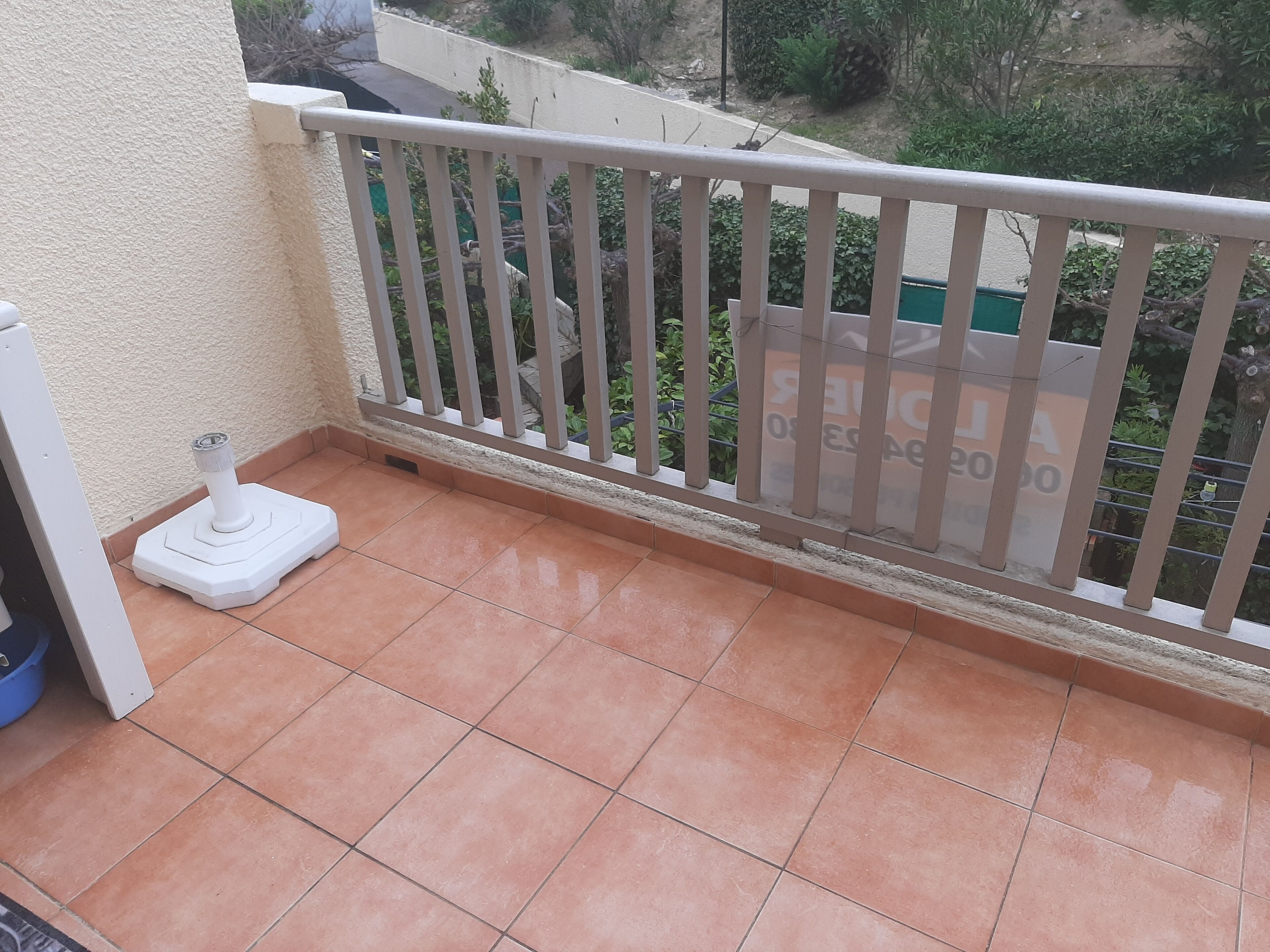 Een balkon met een witte balustrade, een wit voetstuk en een betegelde vloer.