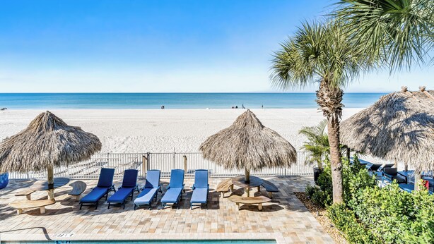 A beachside lounge with blue lounge chairs and thatched umbrellas, overlooking a sandy beach and the sea.