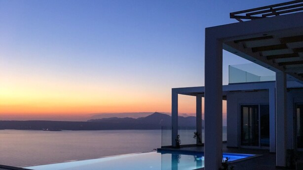 Zona de piscina exterior moderna con vista despejada al mar y montañas lejanas al atardecer.