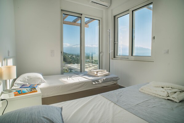 Un moderno cuarto de hotel con dos camas, ventanas amplias, una mesita de noche con lámpara y vistas a las montañas.