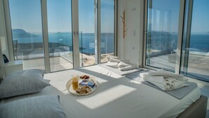 Un dormitorio con una cama grande, una bandeja de desayuno y vista al mar a través de ventanales del piso al techo.