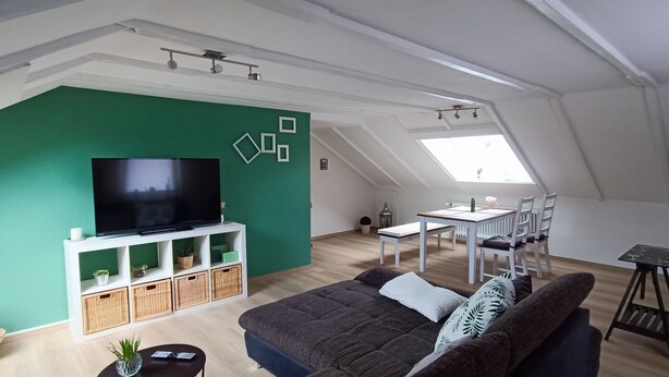 Un soggiorno in stile loft con una parete verde a contrasto, una TV a schermo piatto, un'area pranzo con tavolo e sedie e un angolo salotto accogliente con divano.