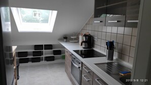 Una cucina moderna con mobili bianchi, forno integrato e macchina da caffè. Sopra il lavello c'è un lucernario e una finestra con vista su un'area verde.