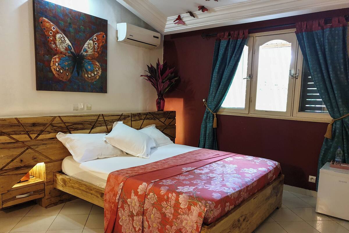 A bedroom with a wooden headboard, a floral bedspread, white pillows, and a painting of a butterfly on the wall.