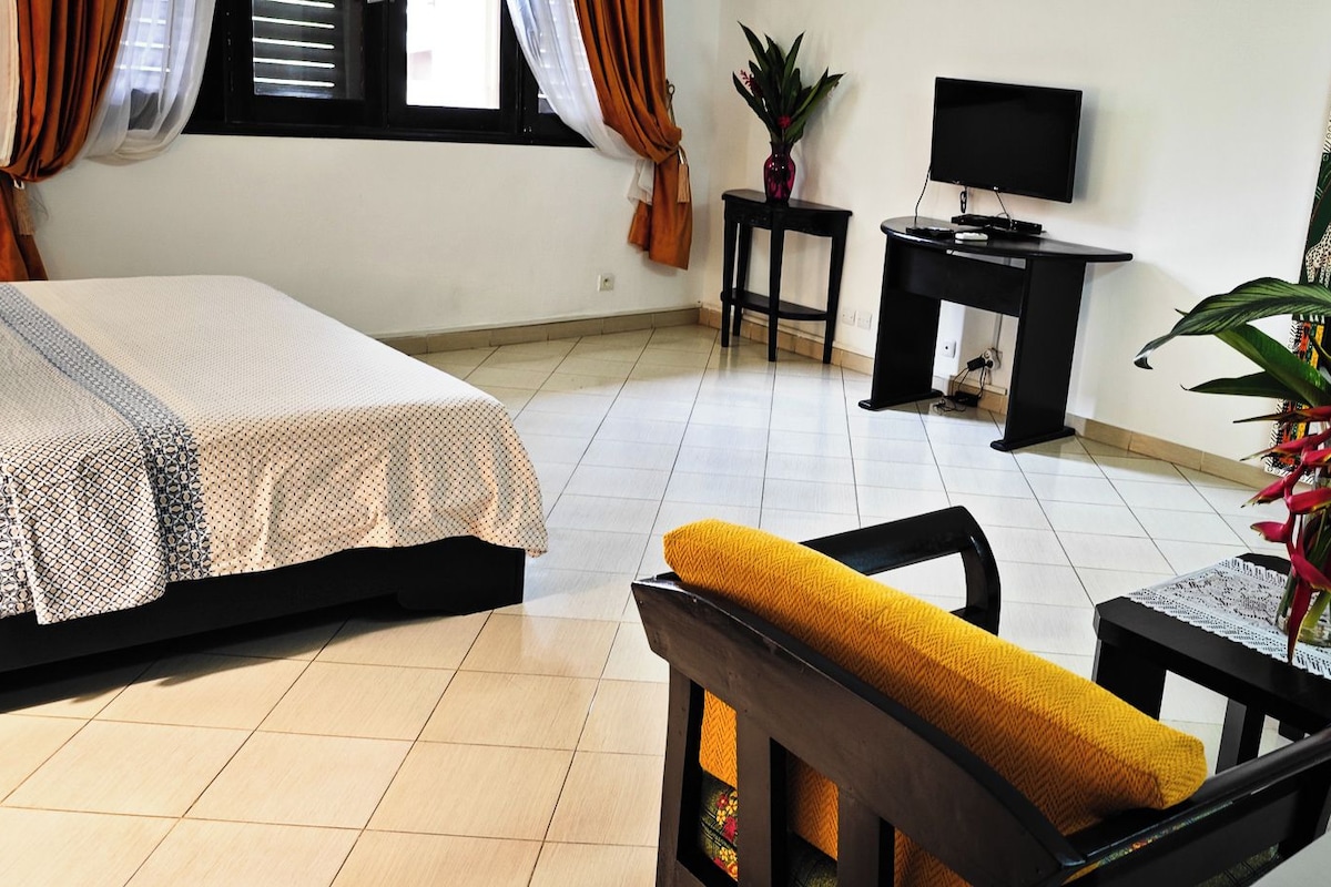 A hotel room with a bed, a TV, a small table, a chair, and a mirror.