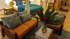 A bedroom with a bed, a wooden nightstand, a bedside table, a sofa, and a decorative plant. - Villa Oasis Abidjan (Abidjan)