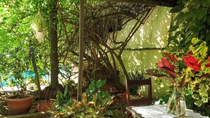 A wooden table with a lace tablecloth, surrounded by lush greenery and a potted plant with red flowers. - Villa Oasis Abidjan (Abidjan)