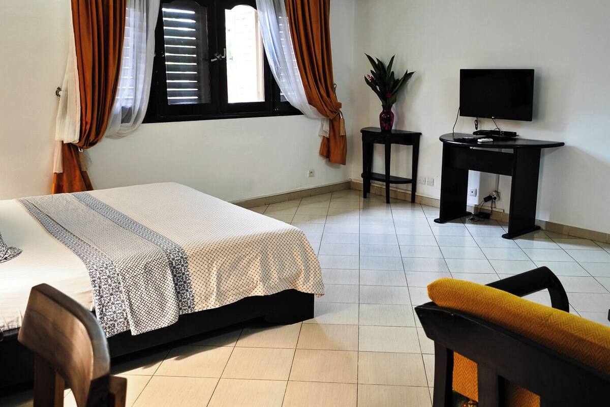 A bedroom with a bed, a desk, a chair, a TV, and a small table.