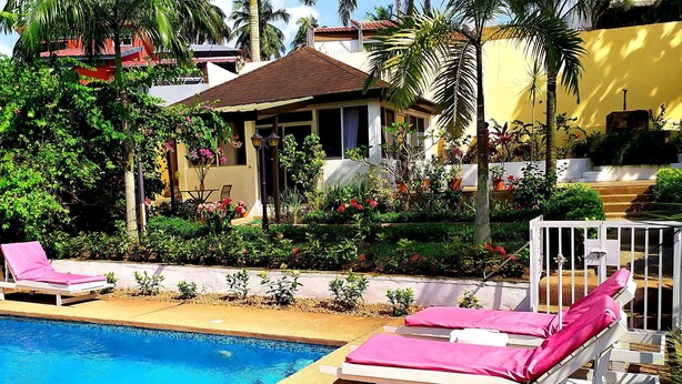 A pool area with lounge chairs and a small house with a red roof. - Villa Oasis Abidjan (Abidjan)