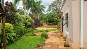A garden pathway leading to a building with a white exterior and a window with a metal frame. - The Berkshire (Harare)