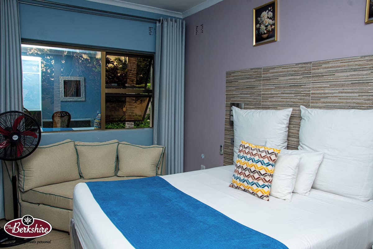 Une chambre à coucher avec un lit, une fenêtre avec des rideaux, un ventilateur et un canapé.