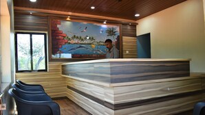 A reception area with a wooden reception desk, a mural with tropical scenery, and a window with a view of trees. - Viraz Valley (Kumta)