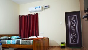 A bedroom with a wooden bed, red curtains, a wall-mounted air conditioner, and a door with decorative paneling. - Viraz Valley (Kumta)