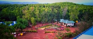 Vista aérea de un hotel con jardín ajardinado, piscina y vistas del bosque circundante.