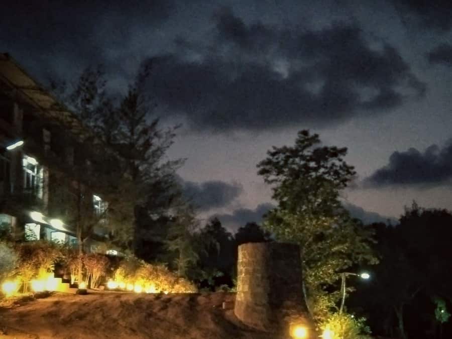 Escena nocturna con una zona de recepción, un sendero de tierra que lleva a un edificio y una estructura de piedra.