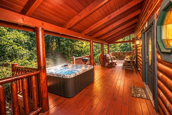 A wooden deck with a hot tub, outdoor seating, and a view of a forested area.