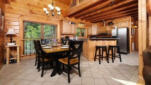 A wooden cabin kitchen with a dining table, chairs, and a refrigerator.