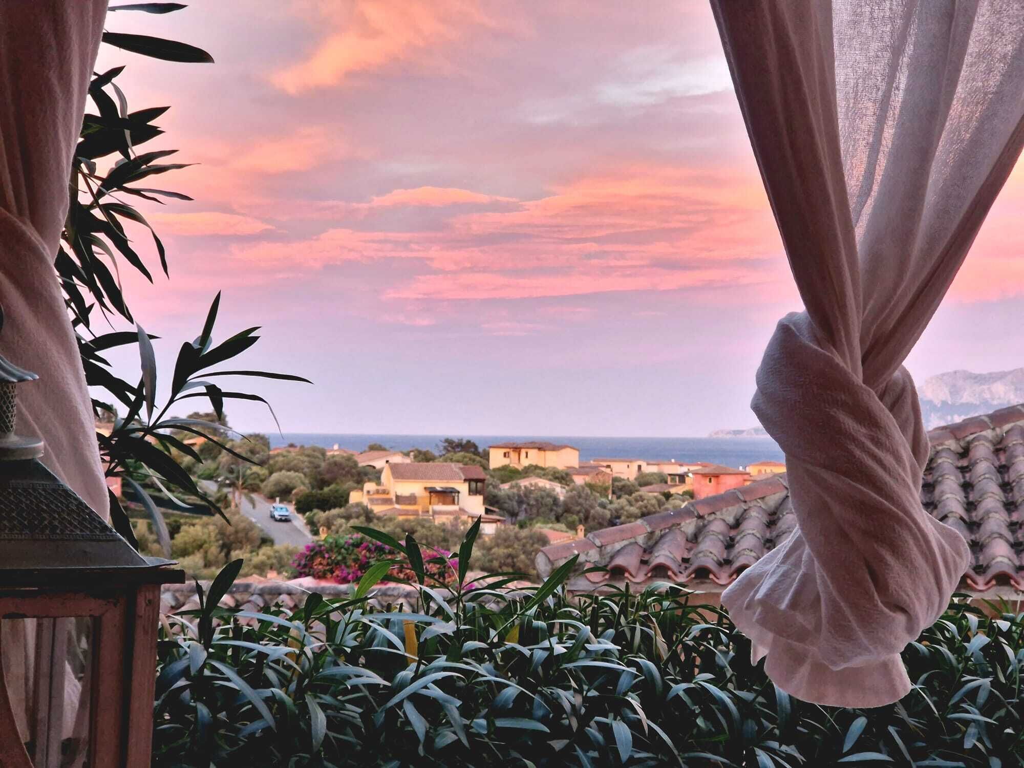 A view from a balcony with a curtain, overlooking a coastal town with houses and a clear sky.