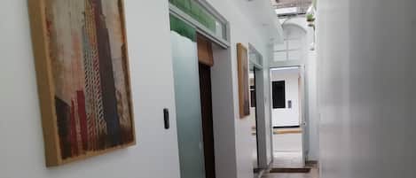 Um corredor com chão de azulejos, um quadro de uma paisagem urbana e uma porta que dá para outro cômodo.