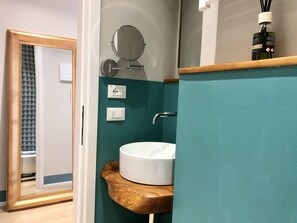 A bathroom with a white sink, a mirror, and a wooden shelf.