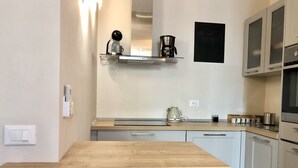 Eine moderne Küche mit Holztisch, weißen Schränken, einer Kaffeemaschine und einem Wasserkocher.