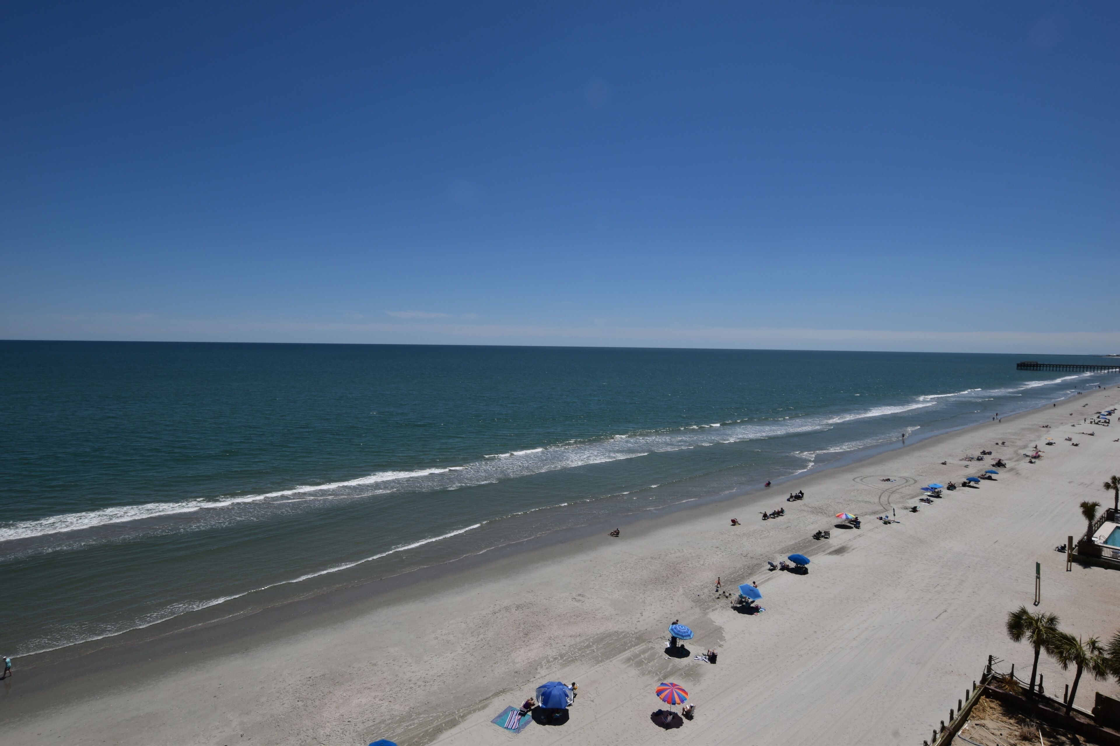 Une plage avec des parasols, une jetée qui se dessine à l’horizon et un ciel dégagé.