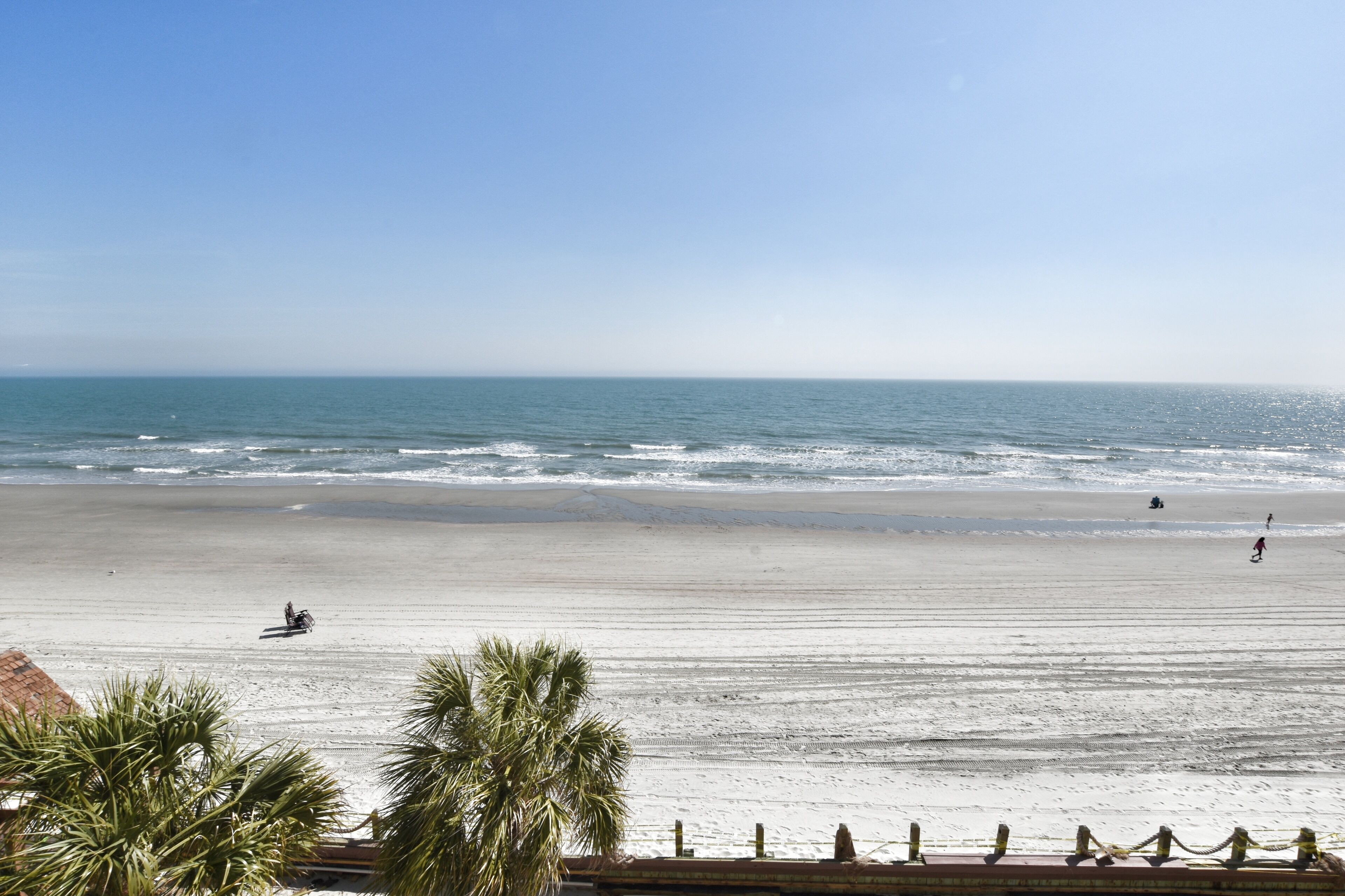 A beach with a clear sky, calm sea, and a few people.