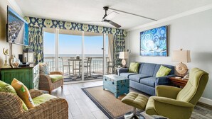 A spacious living area with a balcony, wicker furniture, a blue sofa, and a painting. - 0309 Waters Edge Resort 1 Bedroom Condo by RedAwning (Murrells Inlet)