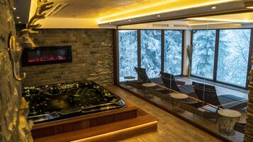 A modern spa area with a stone wall, a hot tub, and a seating area with a view of snow-covered trees.