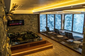A modern spa area with a stone wall, a hot tub, and a seating area with a view of snow-covered trees.