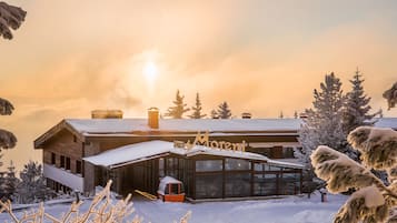 A modern hotel with a glass facade, a ski lift, and a snowy landscape.