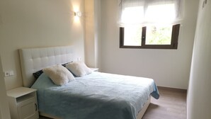 A bedroom with a bed, nightstands, a window with curtains, and a wall-mounted light fixture. - Holiday apartment Lime Javea - Golden star (Xàbia)