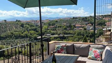 A balcony with a table, two chairs, a sofa, and a large umbrella.