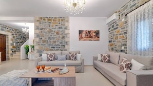 A living room with stone walls, two sofas, a coffee table, and a chandelier. - Villa Nikos - Faraggi Villas (Zoniana)