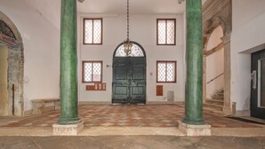A spacious lobby with a checkered floor, a large arched doorway, and green columns. - Apartment Donna Mathilde (Venezia)