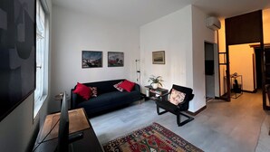 A living room with a dark sofa, red cushions, a small table with a plant, and a colorful rug. There are three framed pictures on the wall. - Apartment Donna Mathilde (Venezia)