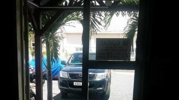 A doorway leading to a parking area with a car parked outside. - Hôtel le corail (Port Louis)