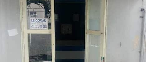 Una puerta que da a un edificio con un letrero que dice "LE CORAIL" y un número de contacto.